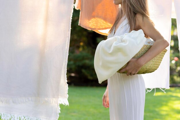 Side view of young woman standing in front of linen laundry in the garden with summer light