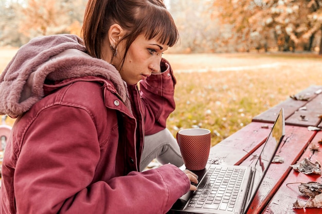 Foto vista laterale di una giovane donna che usa un portatile sul tavolo mentre è seduta in parco