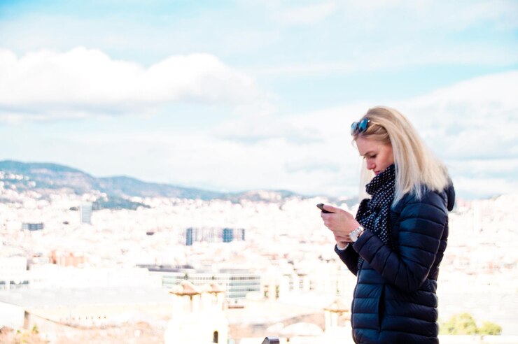 Photo side view of young woman using mobile phone while standing against cityscape