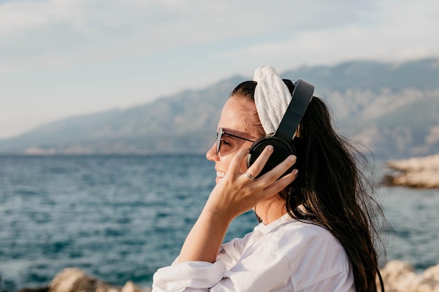 白いシャツを着た若い女性がヘッドフォンで音楽を聴いている横の景色 夏のビーチライフスタイル
