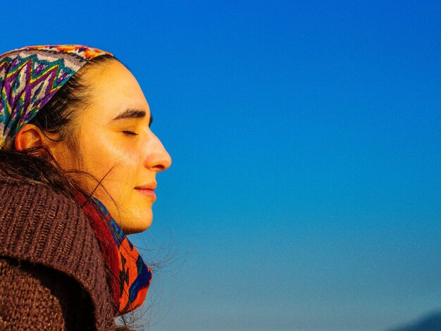 Side view of young woman with eyes closed against clear blue sky