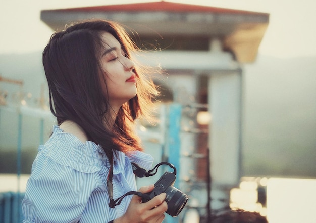 閉じた目でカメラを握っている若い女性のサイドビュー