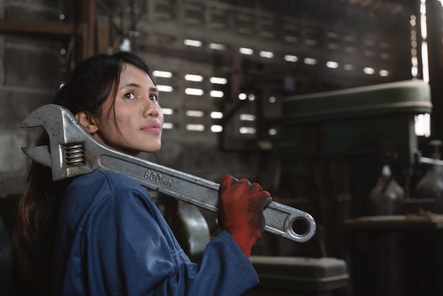 Photo side view of young woman with large wrench standing in factory