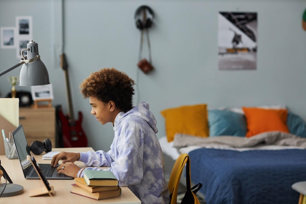 Side view of youthful student sitting by desk in front of laptop