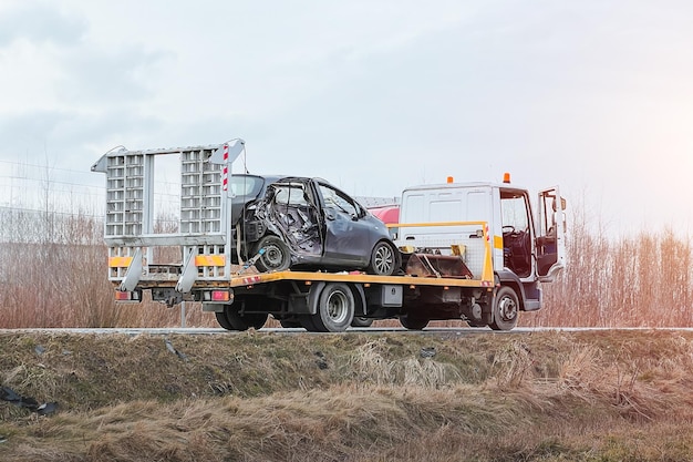 A sideimpact collision leaves a car in need of a tow truck The car is severely damaged and may be beyond repair A modern black Japanese hatchback is being hauled away by a tow truck on the highway