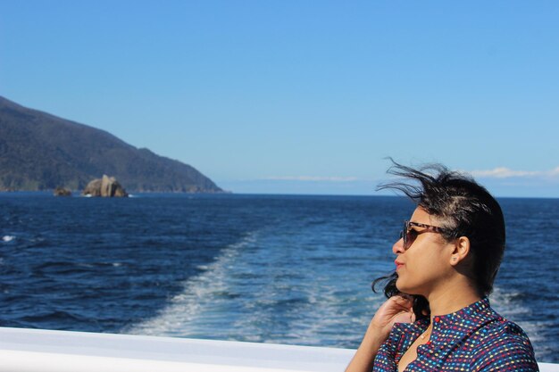 Photo sideview of a woman wearing sunglasss holding her hair against deep blue doughtful sound