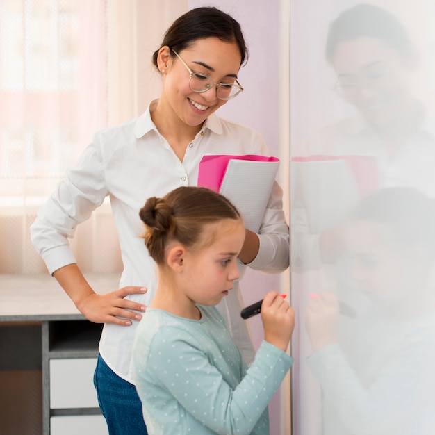 Photo sideways little girl writing on a white board next to her teacher