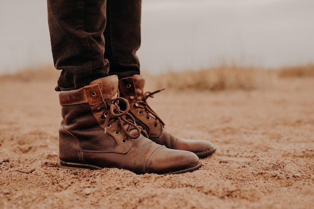 Боковой снимок человека в лохматых коричневых туфлях на лежащей поверхности. Пара ботинок на песке. Мужчина гуляет на свежем воздухе в старой обуви.