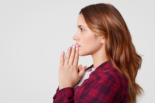 Sideways shot of pretty female keeps hands in praying gesture