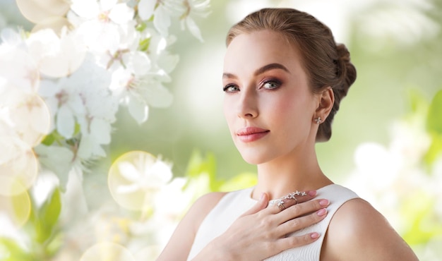 sieraden, luxe, bruiloft en mensen concept - lachende vrouw in witte jurk met diamanten oorbel en ring over natuurlijke lente kersenbloesem achtergrond