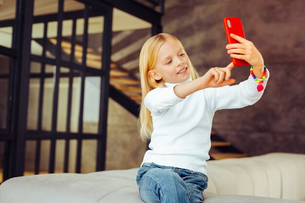 Sieraden voor kinderen. Attente kleuter die haar glimlach demonstreert terwijl ze selfie doet