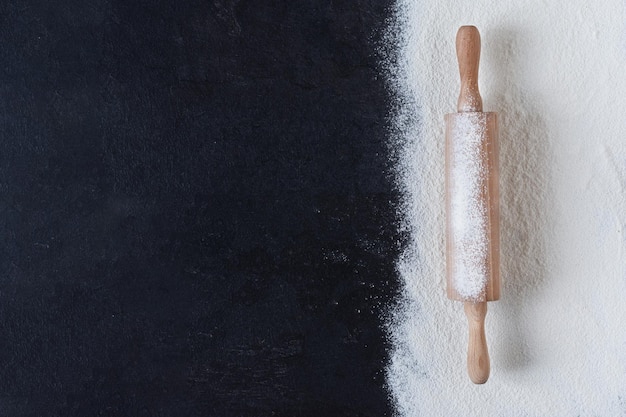 Sifted wheat flour over black surface with rolling pin top view