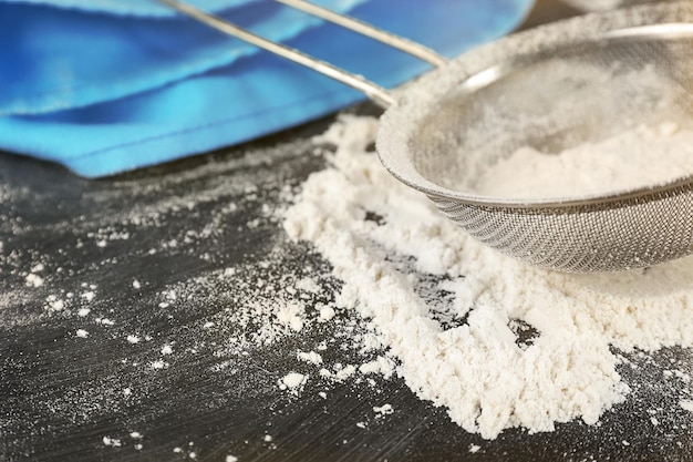 Sifting flour through sieve on wooden table closeup