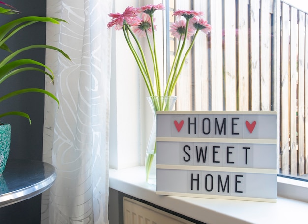 Photo sign home sweet home text on lightbox ,windowsill near window with pink flowers, decorative frame