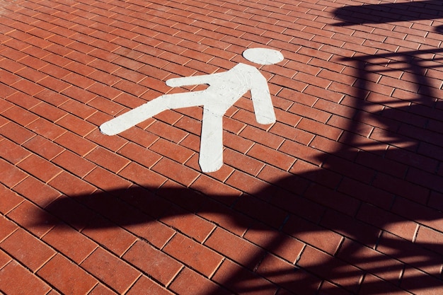 Sign of pedestrian zone in form of white human figure on paving stones and shadow of sitting person