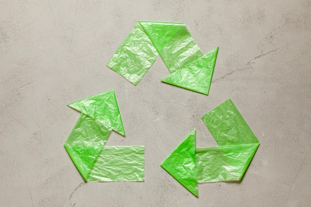 Фото Знак переработки пластика из зеленых пакетов на сером фоне. загрязнение окружающей среды одноразовыми продуктами.