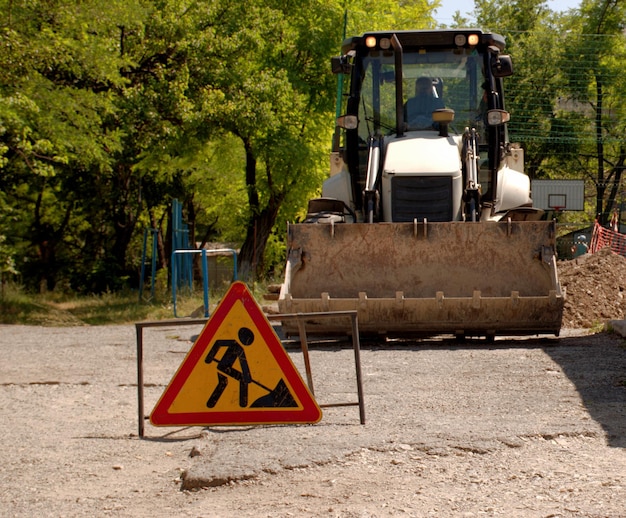 Photo a sign that repairs are underway in the yard in the background there is an excavator with a bucket