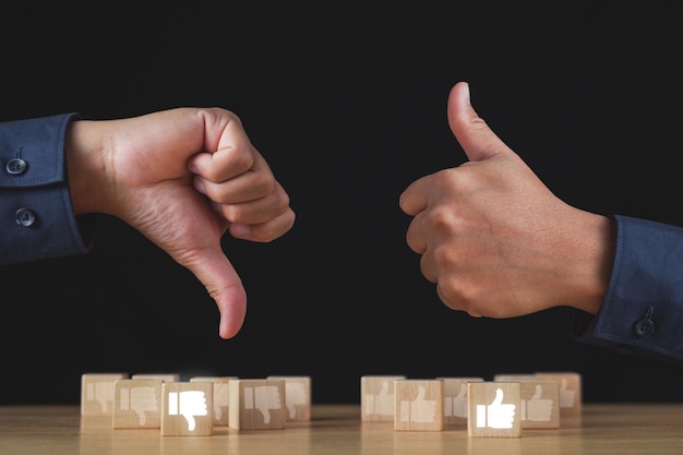 Photo sign of thumbs up and thumbs down to show the like and unlike feeling hands and wood blocks isolated on black background evaluation and satisfaction concept