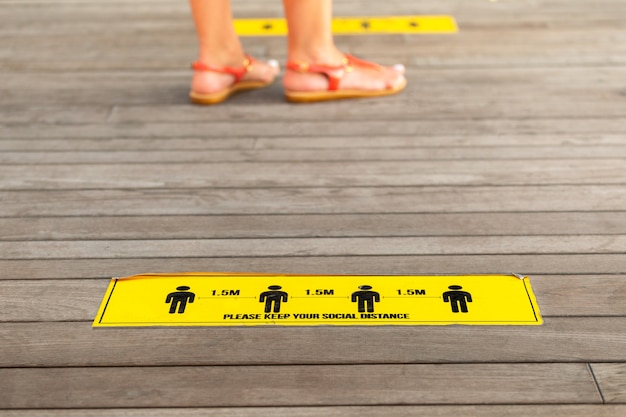 Photo sign with social distance and legs of woman standing on markings for social distancing. selective focus.