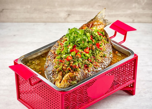 Фирменная рыба со свежим перцем чили в блюде, изолированном на тушеном мясе, вид сбоку на коврике на сером фоне