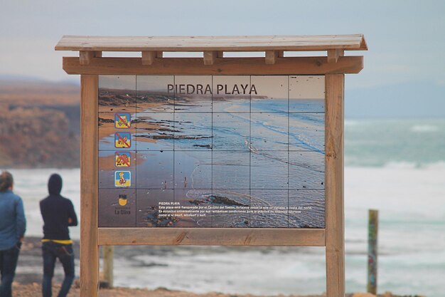 Photo signboard at sea shore against sky