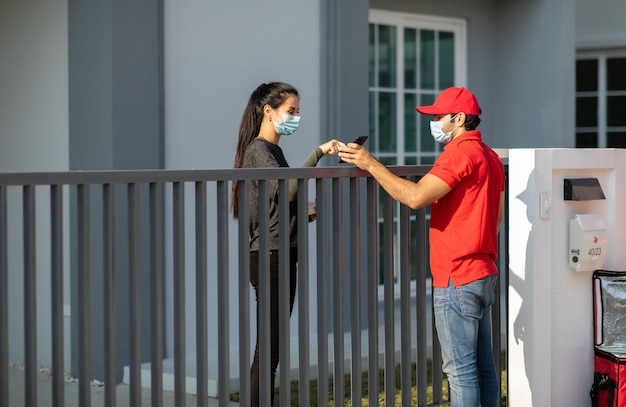 Signing signature on smart phone device to get a package. woman receiving package from delivery man in red uniform .