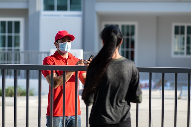 Signing signature on smart phone device to get a package. woman receiving package from delivery man in red uniform .