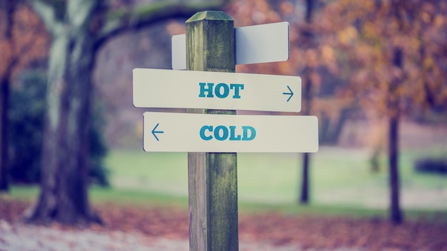 Signpost in a park or forested area with arrows pointing two opposite directions towards Hot and Cold, vintage effect toned image.