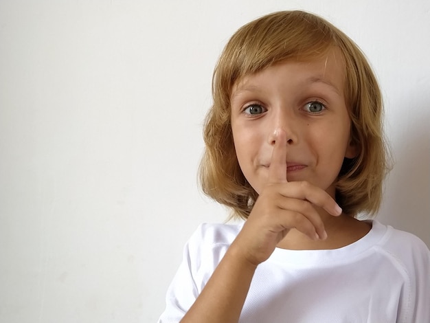 Silence gesture The finger is near the mouth The girl on a white background shows a gesture of keeping silence Child of 7 years old with blond hair Caucasian type Copy space Place for text