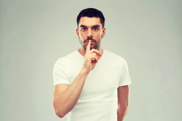 silence, gesture and people concept - young man making hush sign over gray background