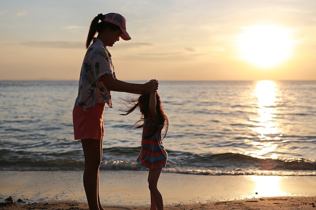 Silhouet Aziatische moeder en dochter die en zich op het strand bij zonsondergang bevinden spelen.