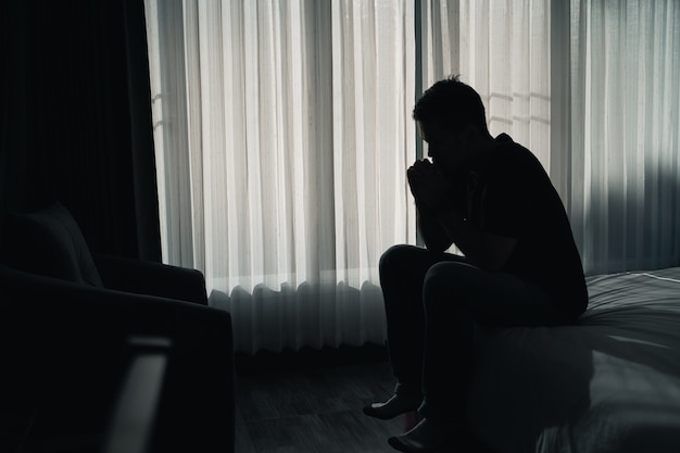 Silhouet depressieve man helaas zittend op het bed in de slaapkamer, depressie concept