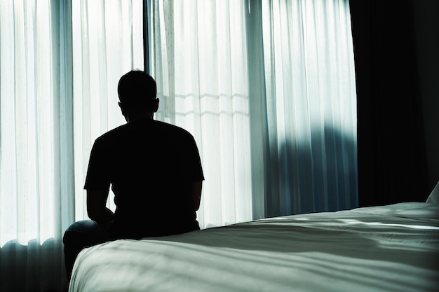 Silhouet depressieve man helaas zittend op het bed in de slaapkamer trieste aziatische man die lijdt aan depressie slapeloosheid wakker en zit alleen op het bed in de slaapkamer depressie gezondheid mensen concept