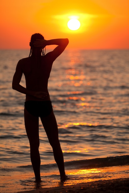 Silhouet die van de mens zich achteruit op zeewaterrand bevinden en van zonsondergang genieten