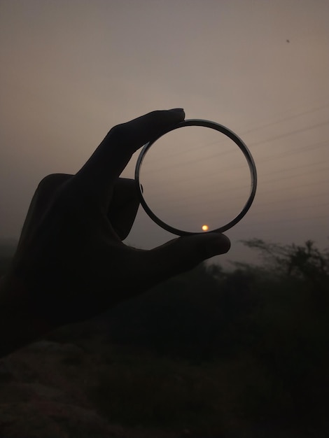 Foto silhouet hand die cirkelvormig glas vasthoudt tegen de hemel tijdens zonsondergang