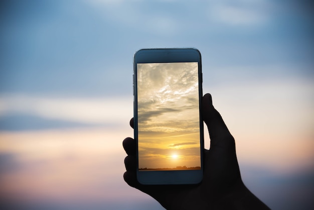 Silhouet hand met smartphone foto nemen in de zonsondergang.