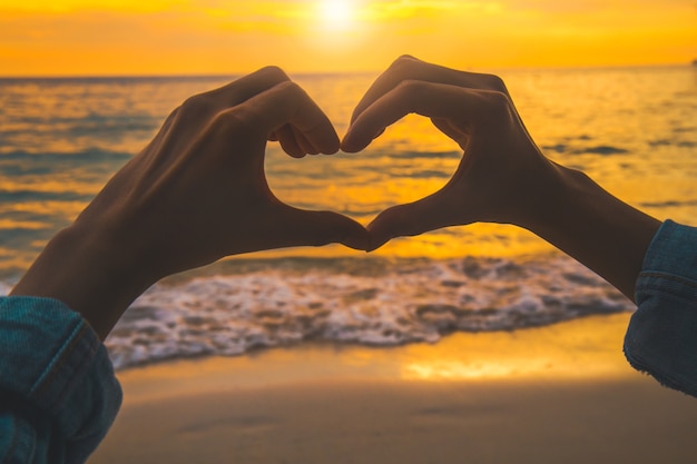 silhouet hartvorm met de hand op het strand bij zonsondergang.