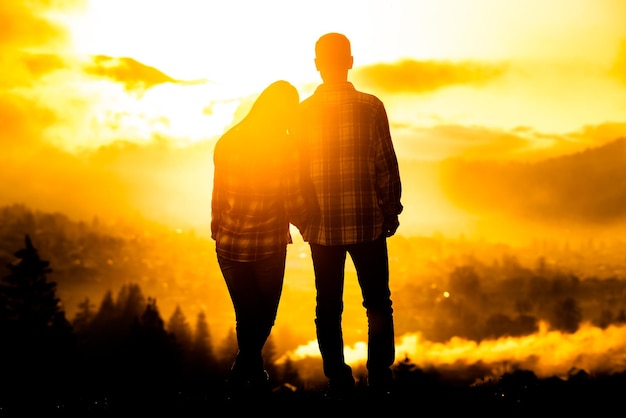 Silhouet jong koppel geliefden omarmd en kijken naar het prachtige berglandschap bij zonsopgang