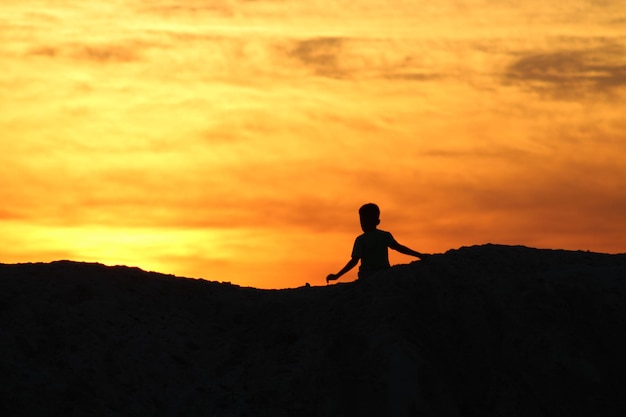 Silhouet jongen staat tegen de hemel tijdens de zonsondergang