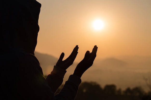 Silhouet man die bidt tegen de hemel bij zonsondergang