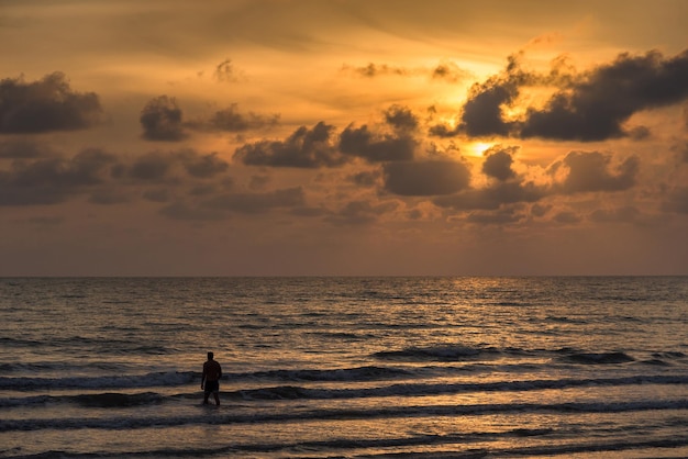 Silhouet man die in de zee loopt tegen zonsondergang