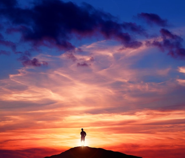 Foto silhouet man die op de berg staat tegen een bewolkte hemel tijdens de zonsondergang