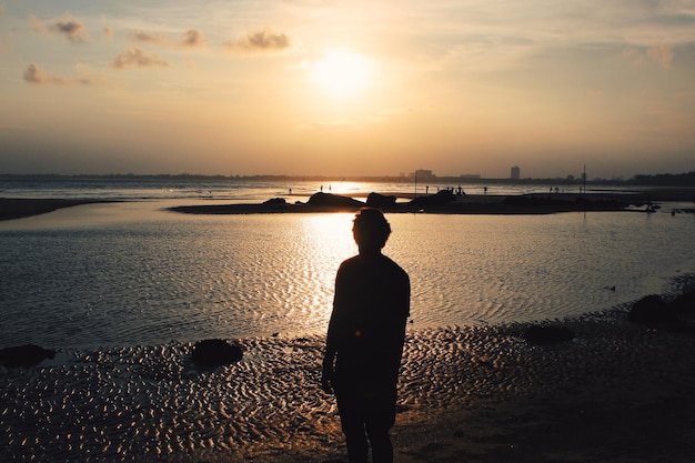 Silhouet man die op het strand staat tegen de hemel tijdens de zonsondergang