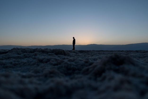 Silhouet man die op het strand staat tegen de hemel tijdens de zonsondergang