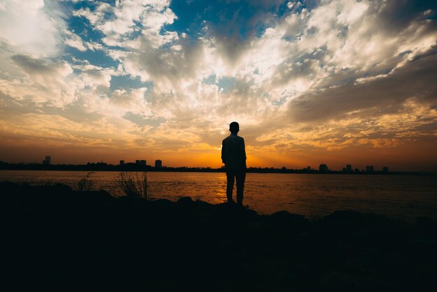 Silhouet man die op het strand staat tegen de hemel tijdens de zonsondergang