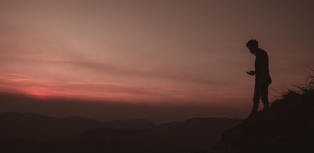 Silhouet man die tijdens de zonsondergang op de berg tegen de hemel staat