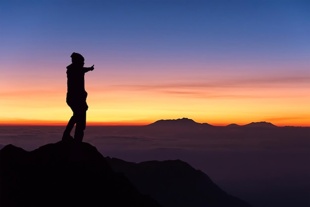 Silhouet man die tijdens de zonsondergang op de berg tegen de hemel staat