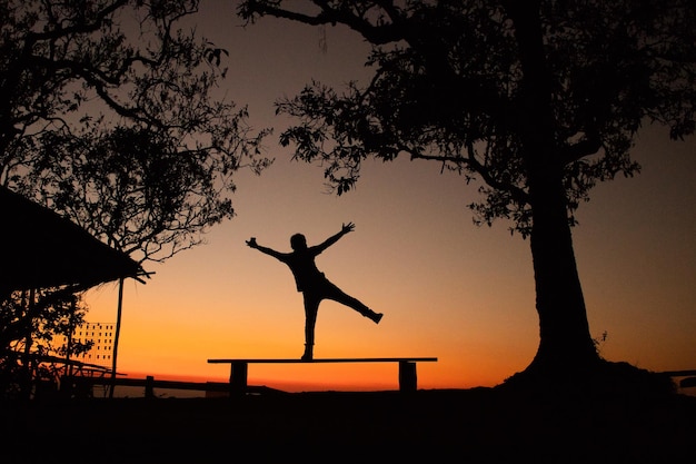 Foto silhouet man die tijdens de zonsondergang op een bankje tegen de hemel staat