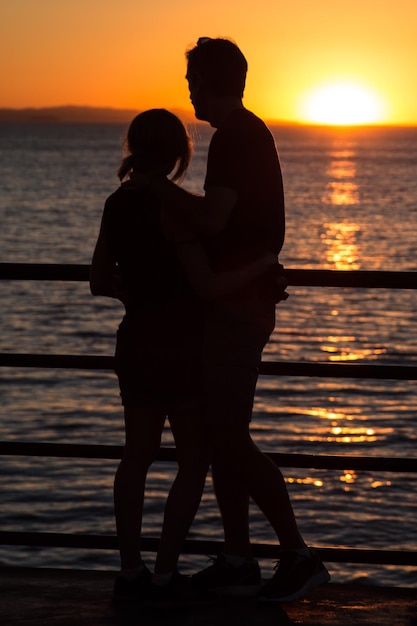 Silhouet man en vrouw staan op de pier bij de zee tegen de hemel tijdens de zonsondergang