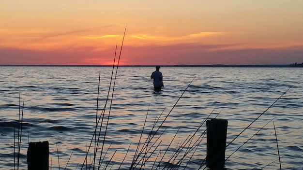 Silhouet man in de zee tegen oranje hemel tijdens zonsondergang